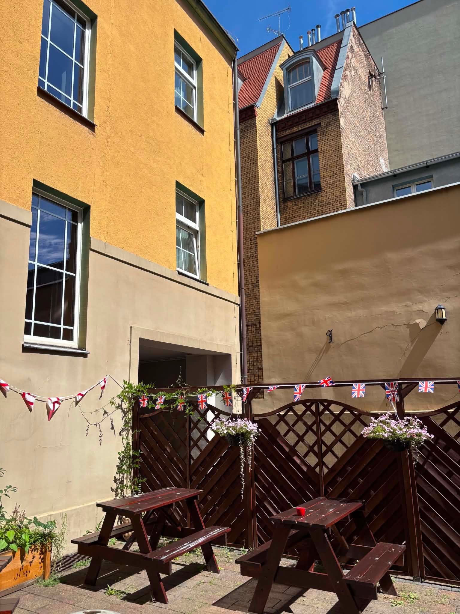 Ogródek na podwórku RoyalPub Poznań — drewniane stoły i brytyjskie chorągiewki